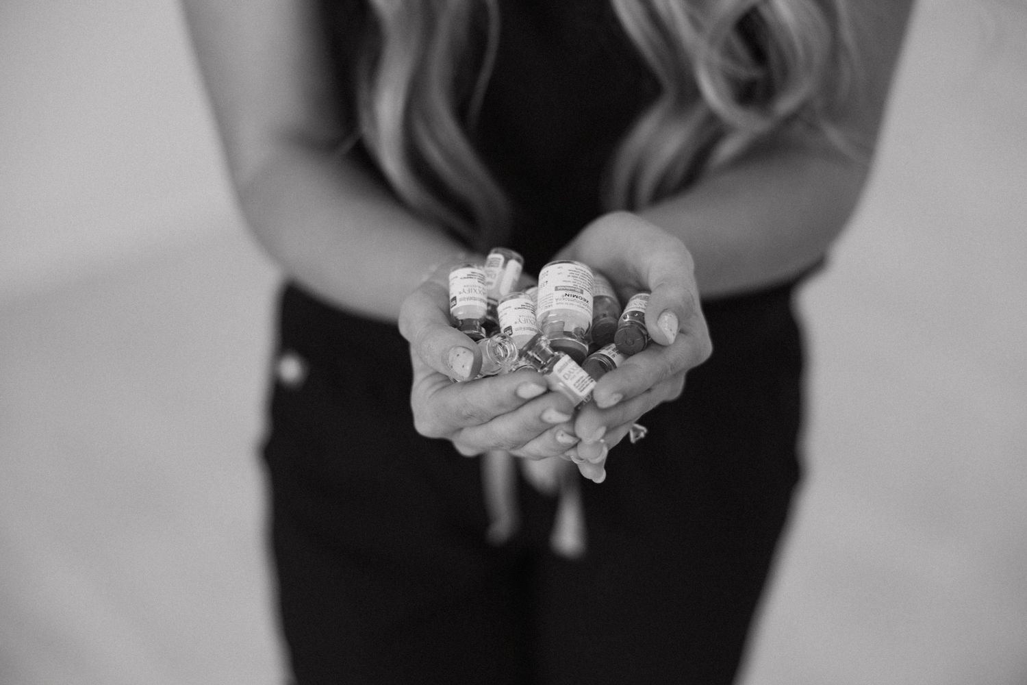Black and white image showing hands holding small objects against dark clothing.