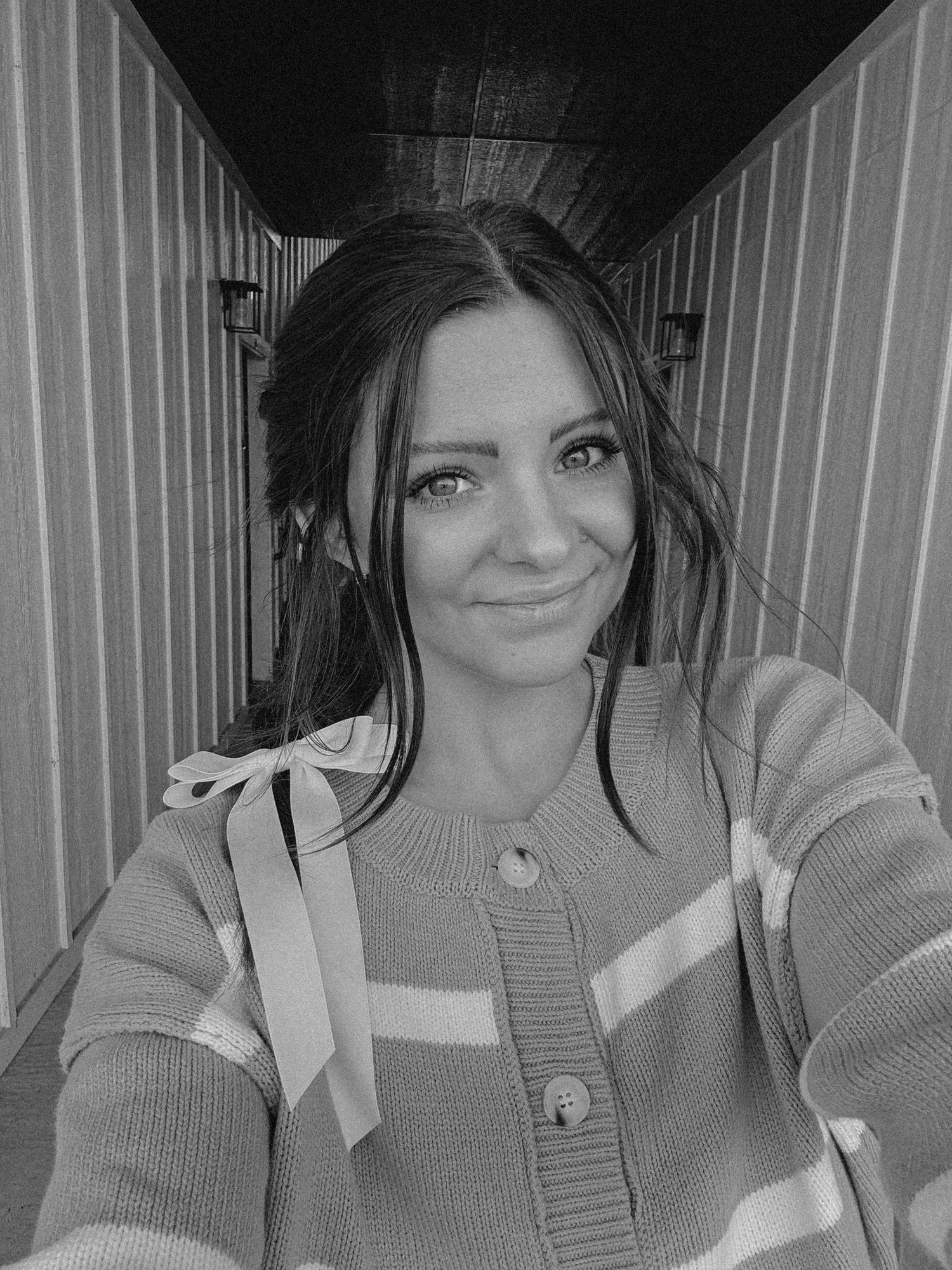 Black and white portrait in a hallway wearing striped sweater.