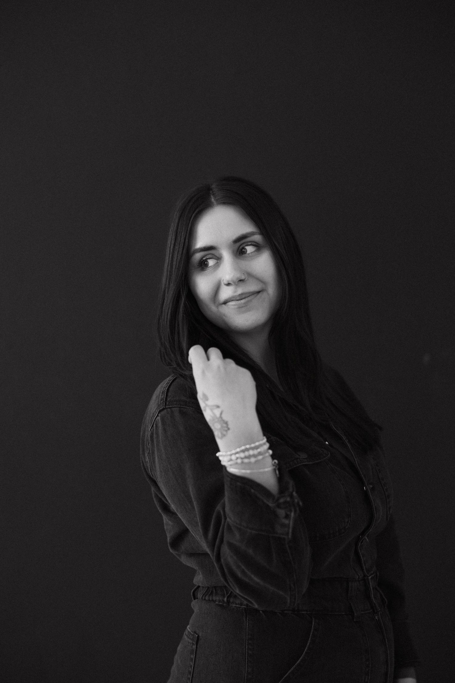 Person in black attire makes expressive gestures against dark studio backdrop.
