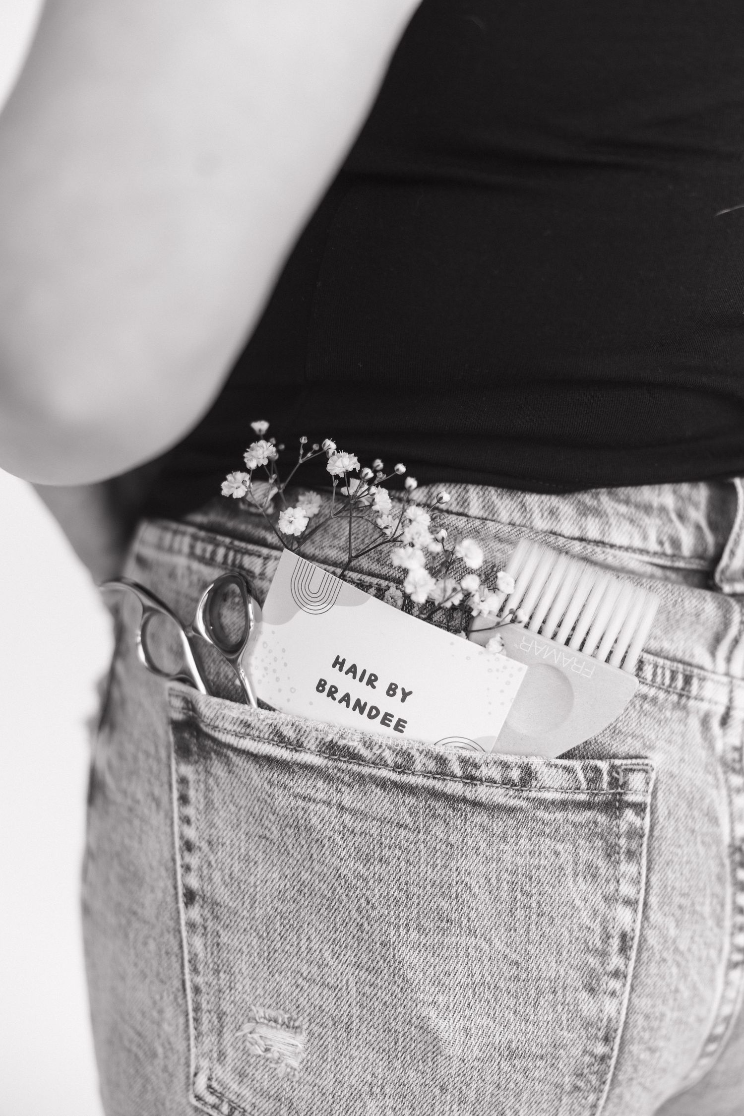 Hair styling tools and business card tucked into a distressed denim pocket.