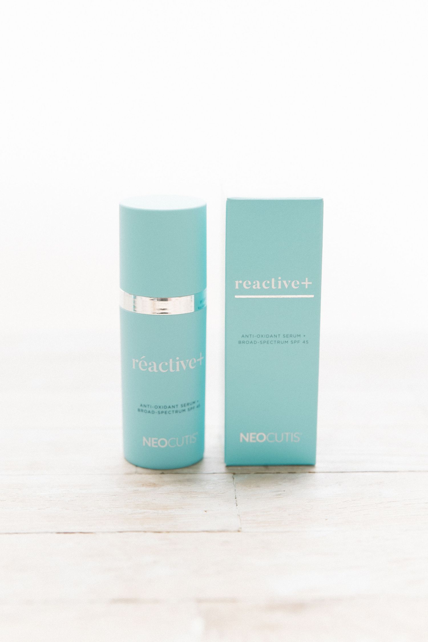 A light turquoise beauty product bottle and packaging box from Reactive+ brand on a white surface.