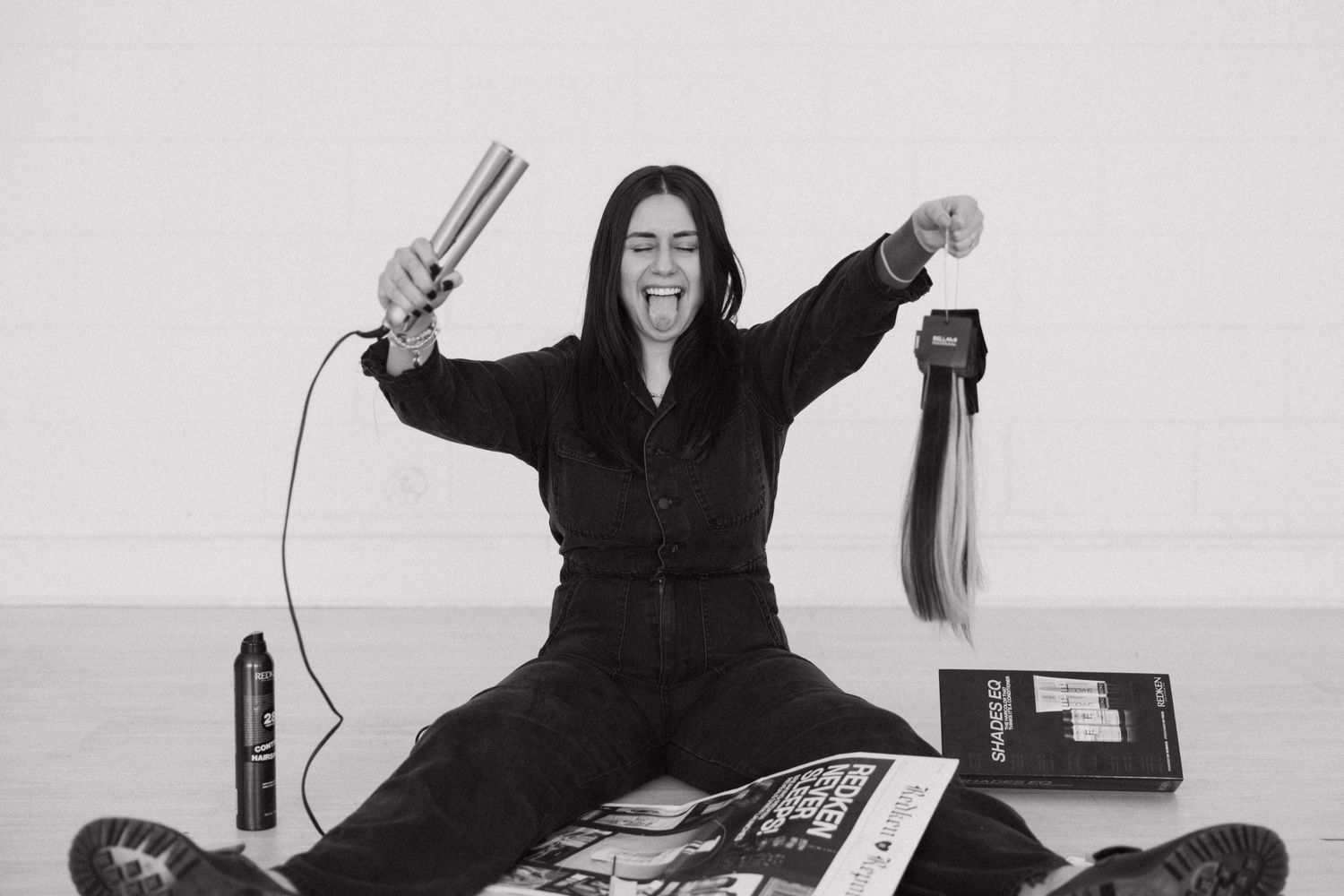 Person in black outfit lying on floor with magazines and hairbrushes.