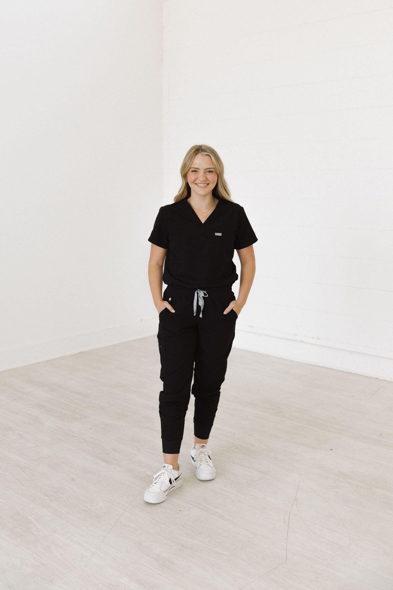 Medical professional in black scrubs and white sneakers standing in bright room.