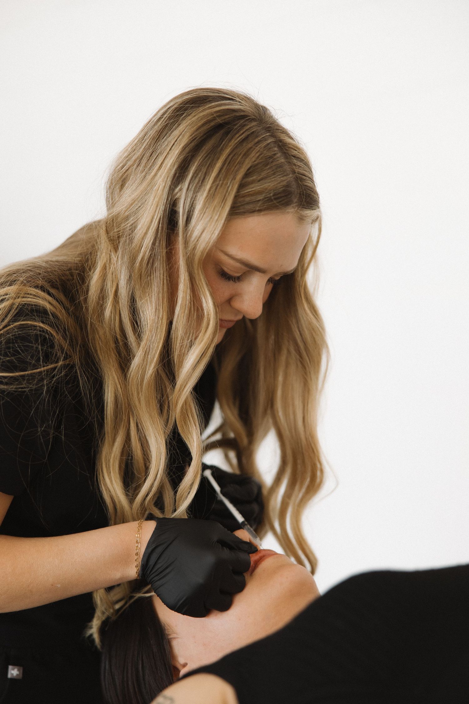 Esthetician in black attire concentrating during cosmetic procedure.