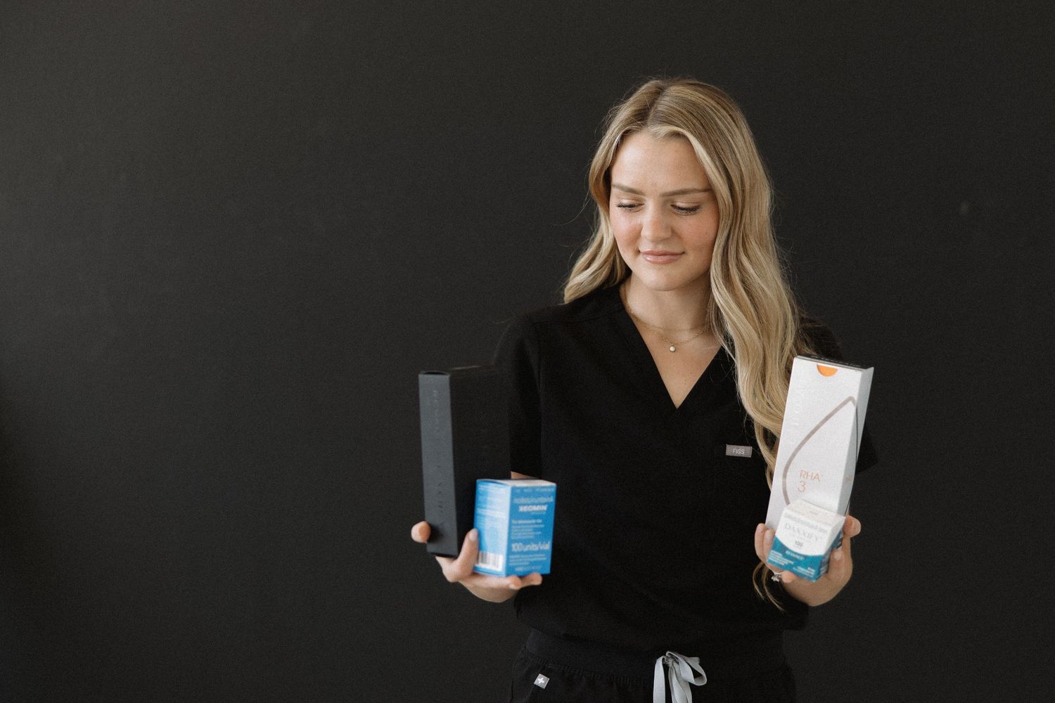 Healthcare worker displays medical products against black wall.