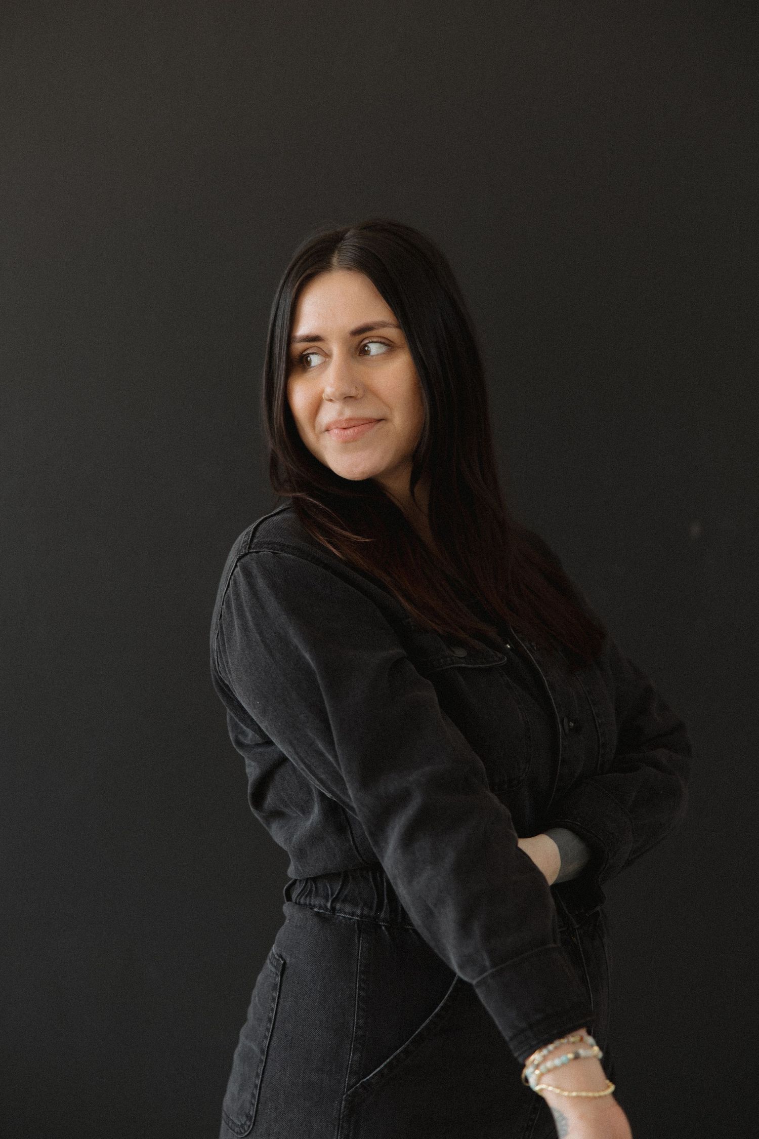 Figure in dark denim jacket poses expressively against black background.