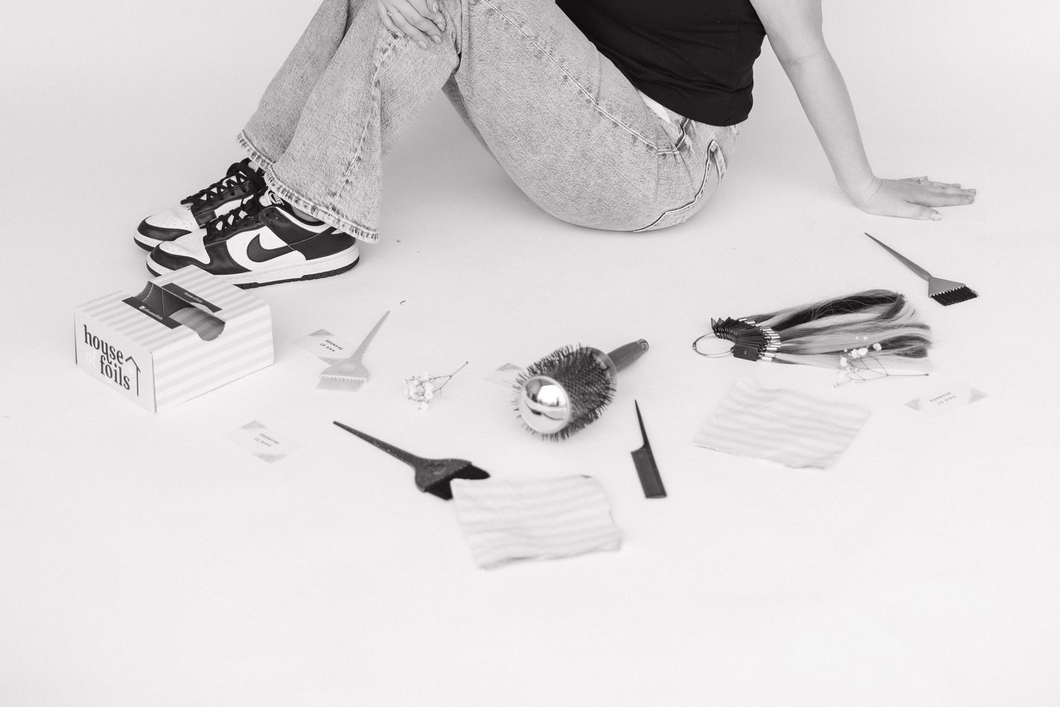 Styling tools and business cards arranged on floor next to person wearing nikes and denim.
