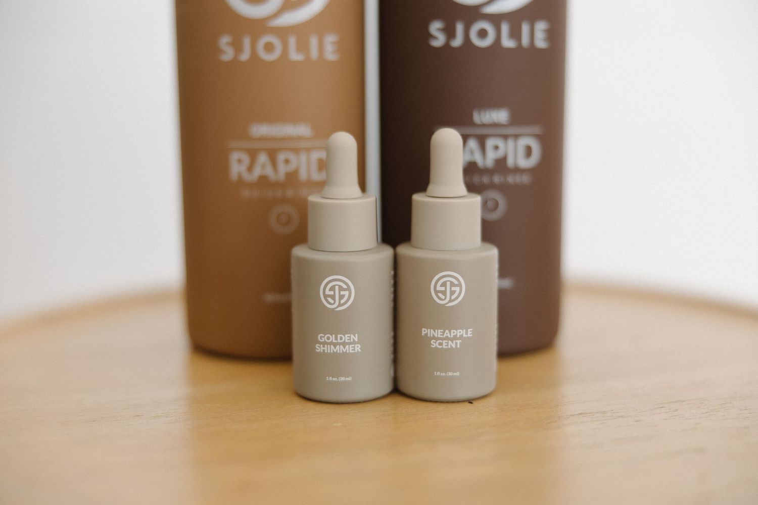 Close-up of Sjolie tanning solution bottles with droppers on wooden table.