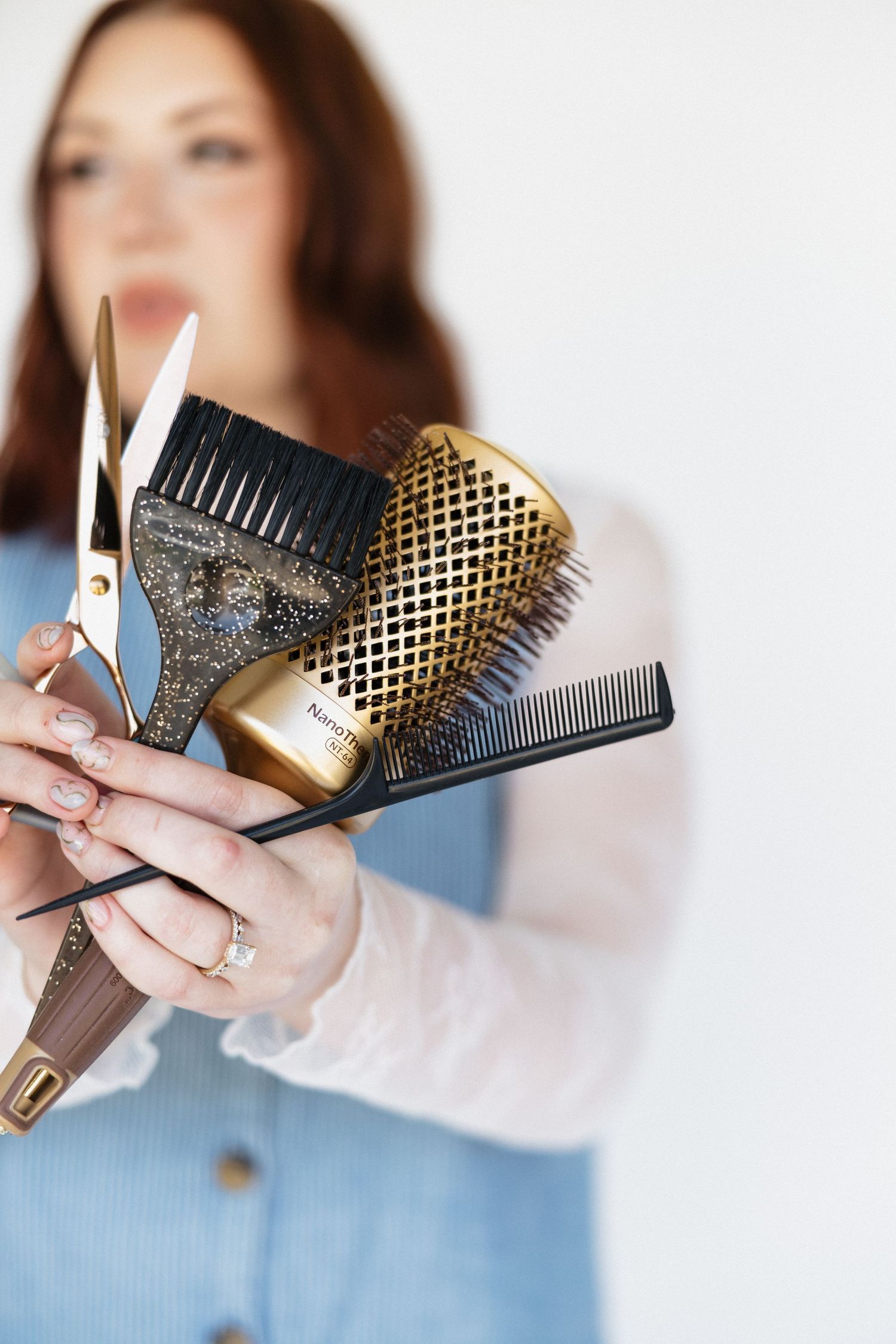 Professional hair styling tools including brushes, combs and scissors held against a white background.