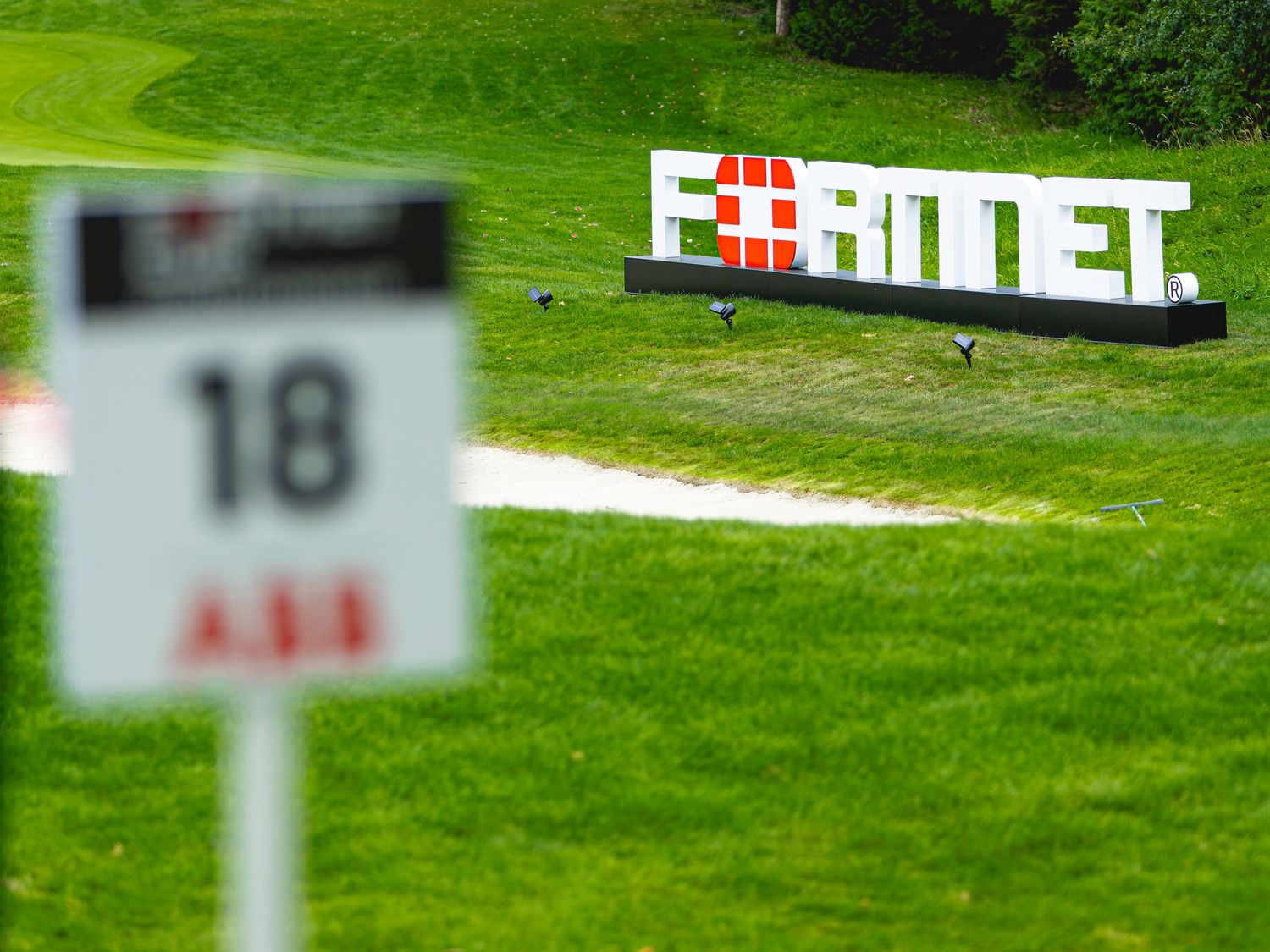 Fortinet logo sign on a lush green golf course fairway near hole 18 with ABB sponsor marker in foreground.