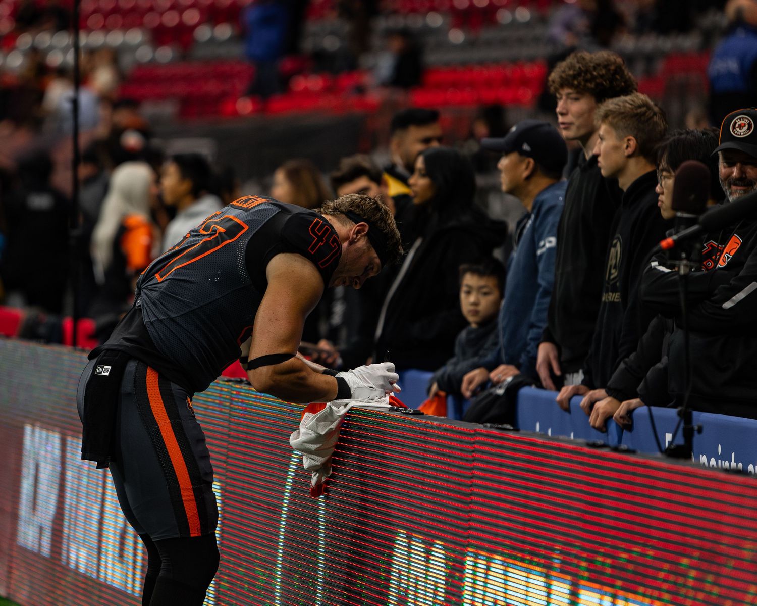 NFL player signing autographs for fans at stadium sideline during game day event.