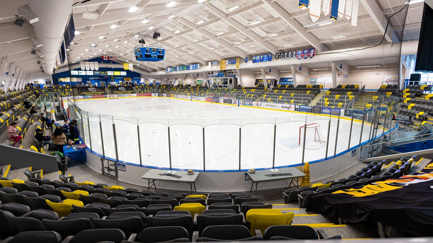 Indoor ice hockey arena with yellow seats, clear rink boards, and bright overhead lighting in a modern sports facility.