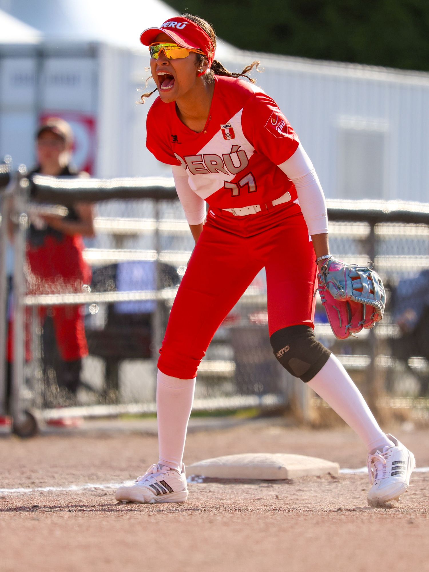 Peru softball player in red uniform celebrates at base during competitive game.