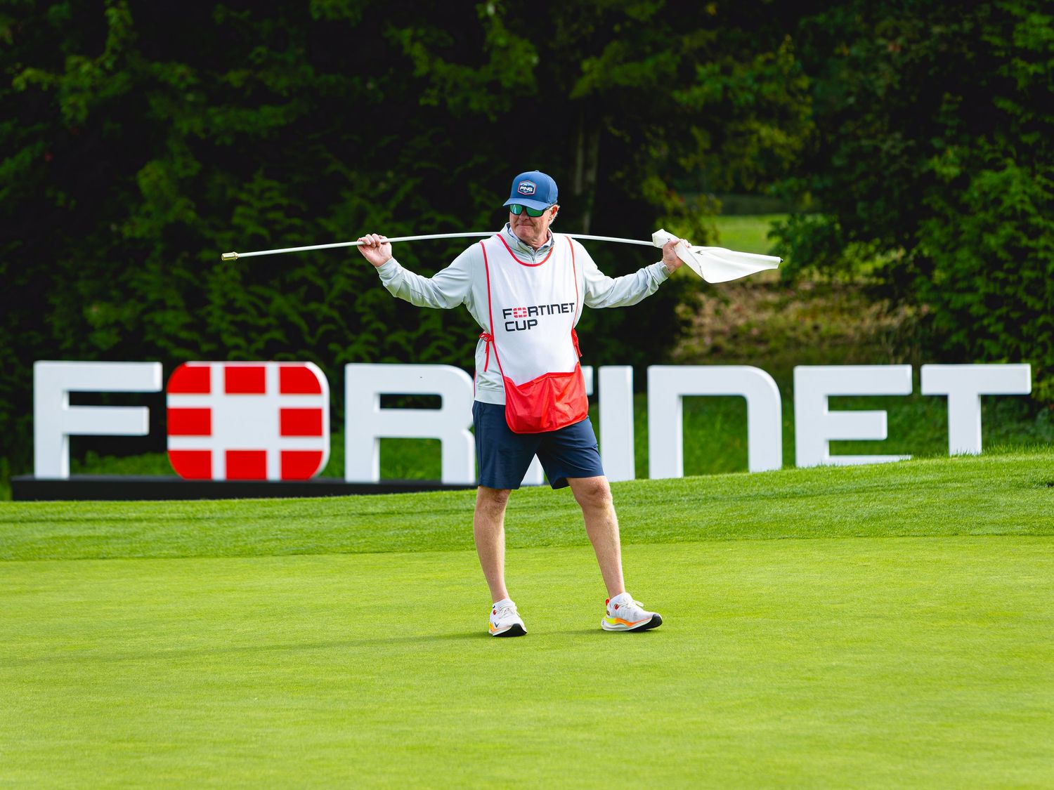 A caddie holds a flag stick on a lush green golf course at the Fortinet Cup tournament.