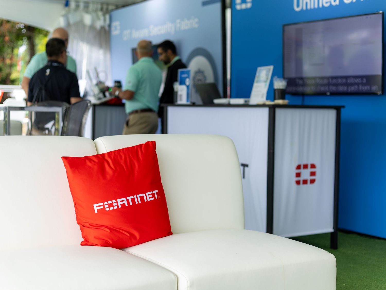 Fortinet branded red pillow on white sofa at a cybersecurity conference booth with Security Fabric signage.