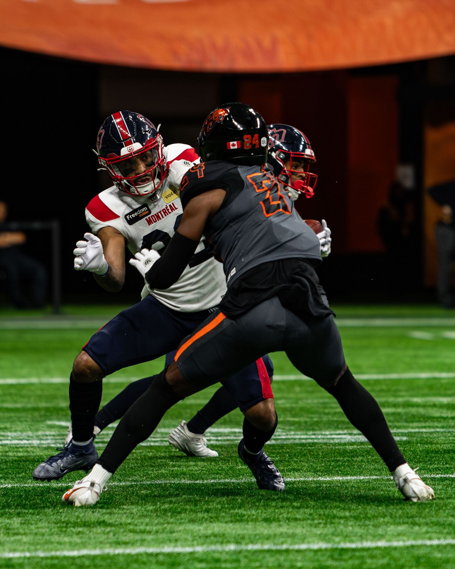 Two American football players clash on the field during a night game, one in white and red, the other in black and orange.