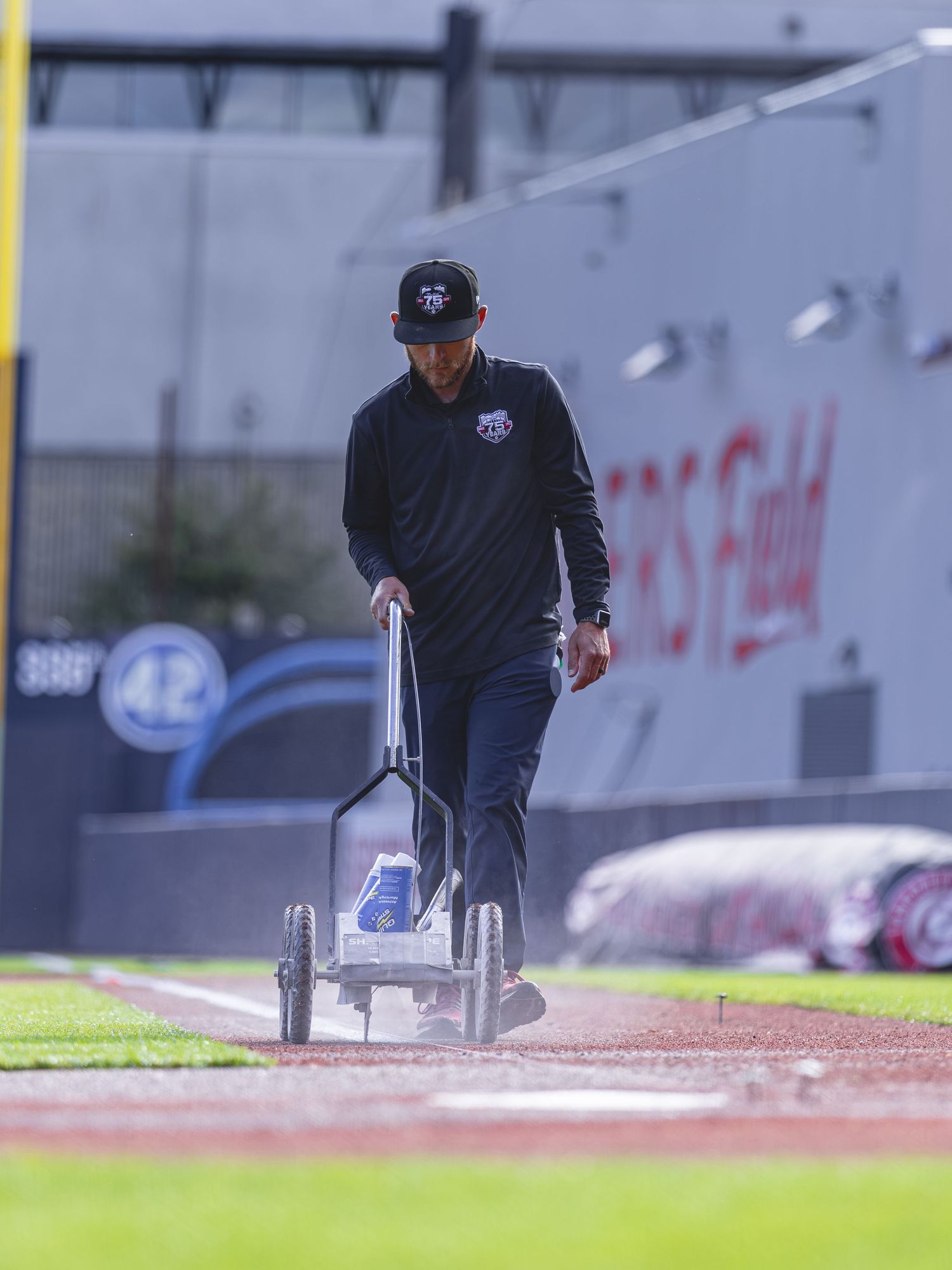 Groundskeeper painting white foul lines on a baseball field using a line striping machine at a stadium.