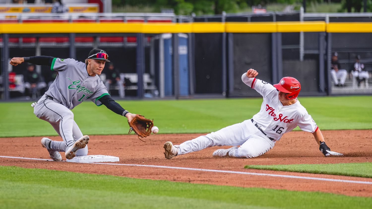 Baseball player slides into third base as fielder reaches to make the tag during an action-packed minor league game.