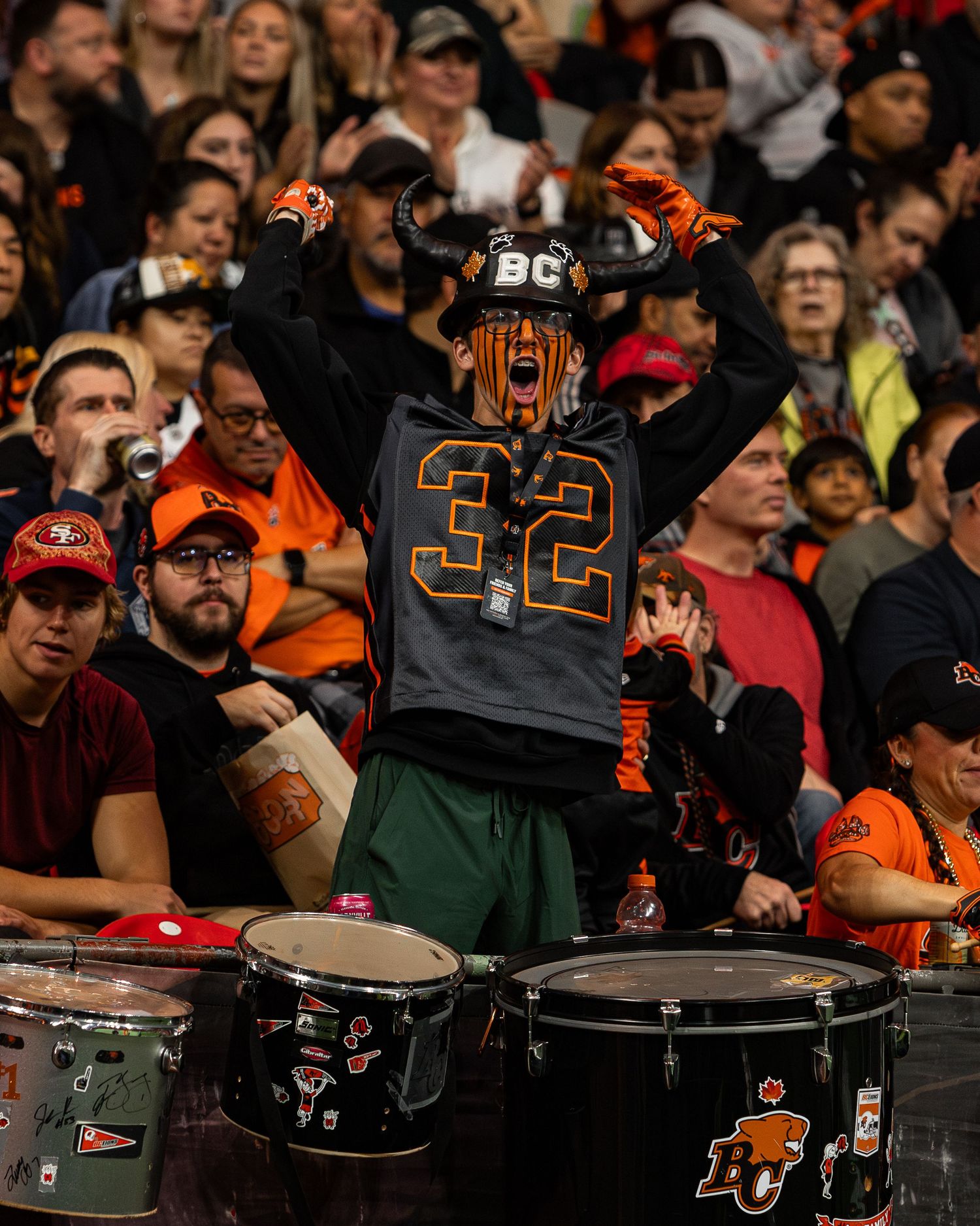 Enthusiastic BC Lions fan in jersey #32 and viking hat cheering loudly at a CFL football game.