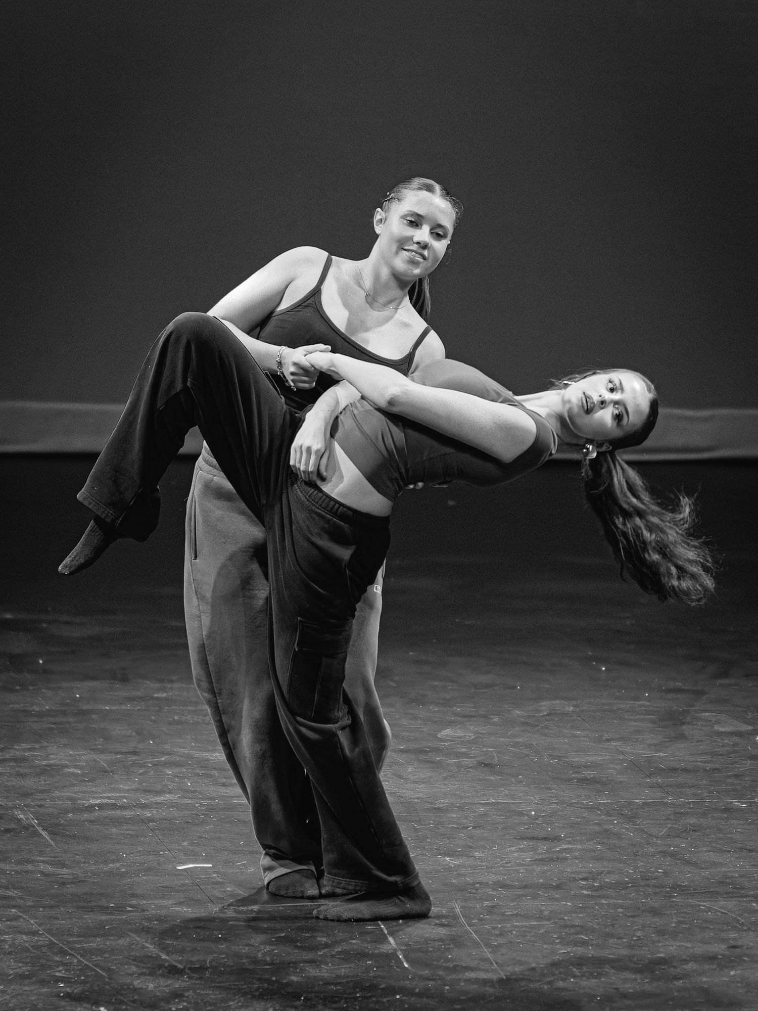 Two female dancers perform a dramatic lift pose on stage in a black and white dance performance photo.