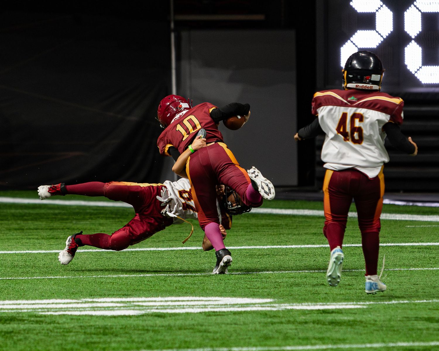 Football players in maroon and gold uniforms compete during an indoor game, with player 10 making a dynamic play.