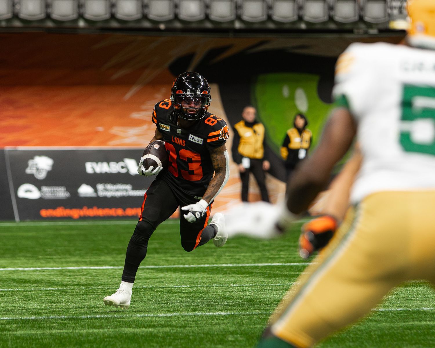 BC Lions player in dark uniform runs on field during CFL game against Edmonton Elks in green uniforms.