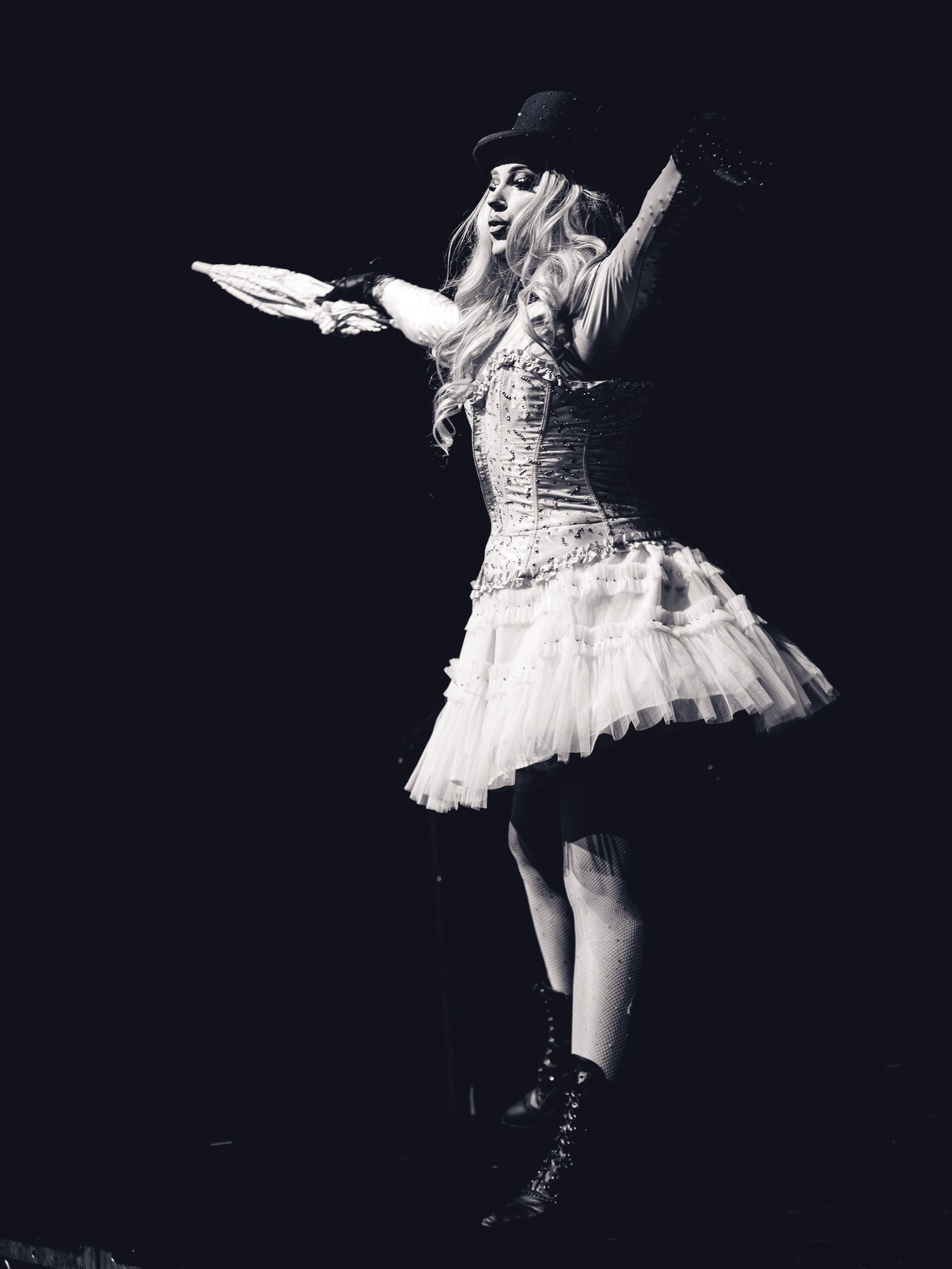 Black and white photo of a woman in a tutu dress, corset, cowboy hat, and boots, dancing on stage.
