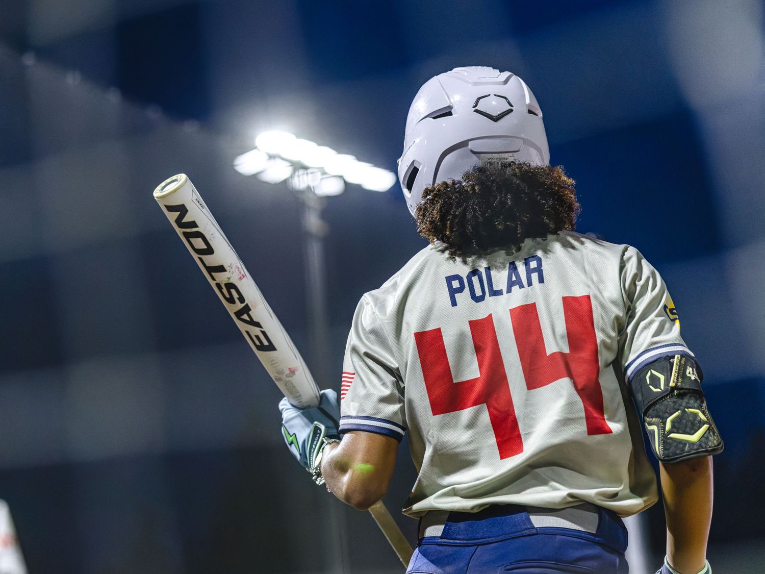 Softball player #44 Polar holds a bat under stadium lights, wearing a white helmet and jersey.