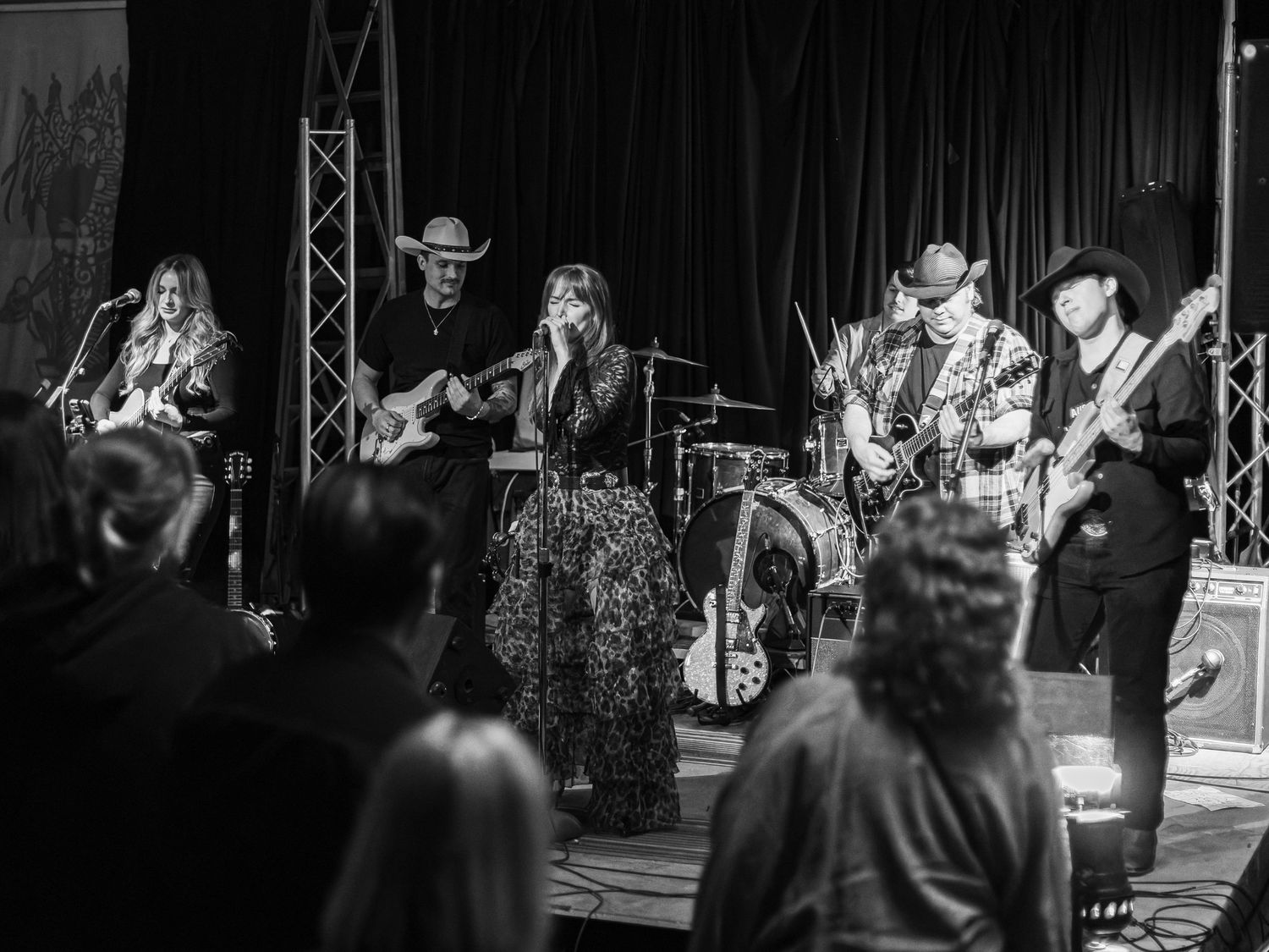 Black and white photo of a country band performing on stage with guitars, drums, and cowboy hats for a live audience.