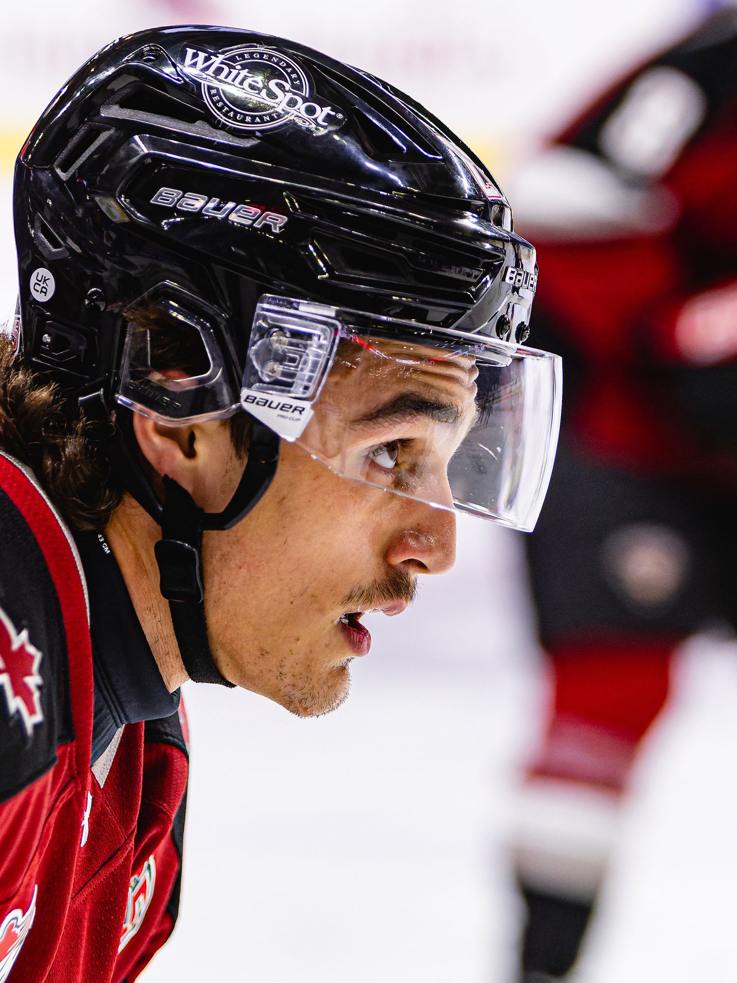 Hockey player wearing a Bauer helmet with visor and White Spot sponsored jersey during an ice hockey game.