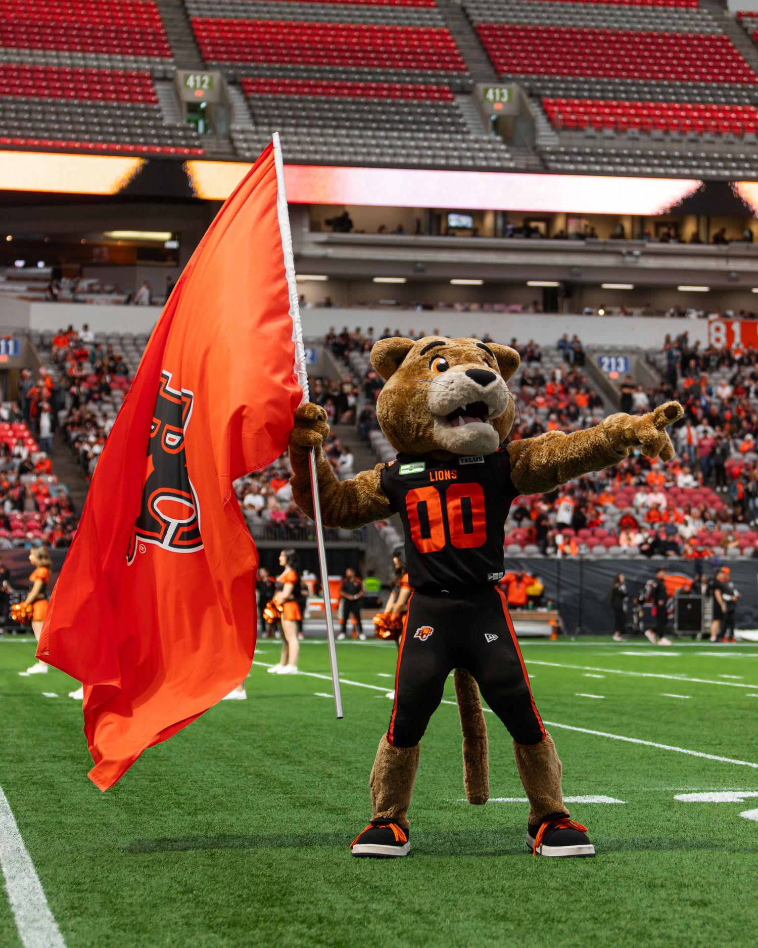 BC Lions mascot Leo holds an orange team flag on the field at BC Place stadium during a CFL game.