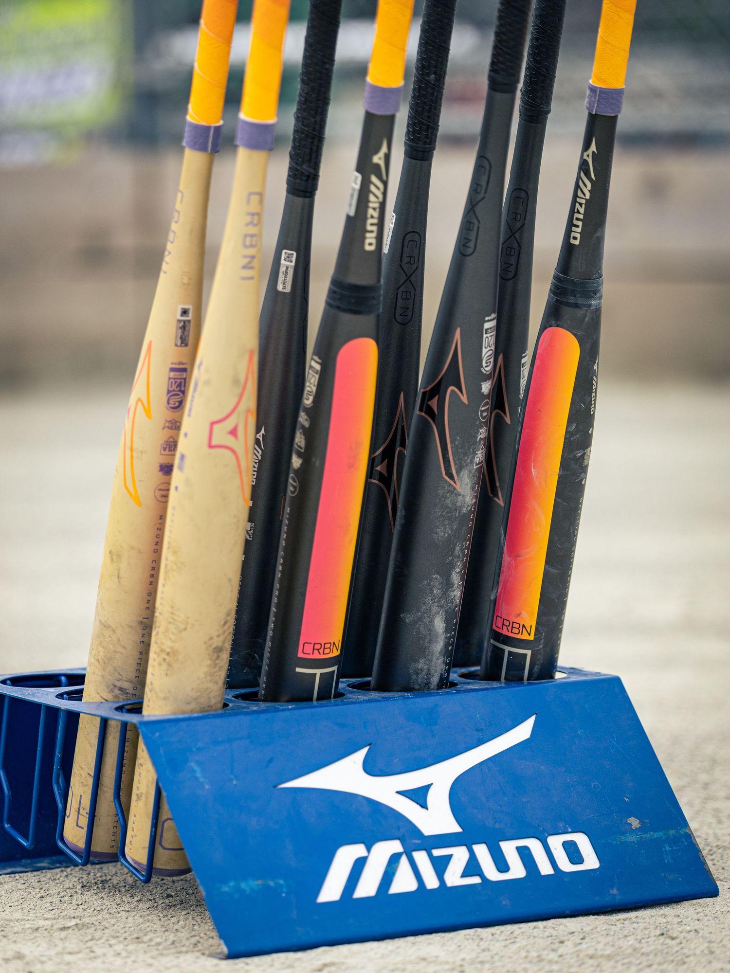 Mizuno baseball bats displayed in a blue Mizuno bat rack on a dugout floor.