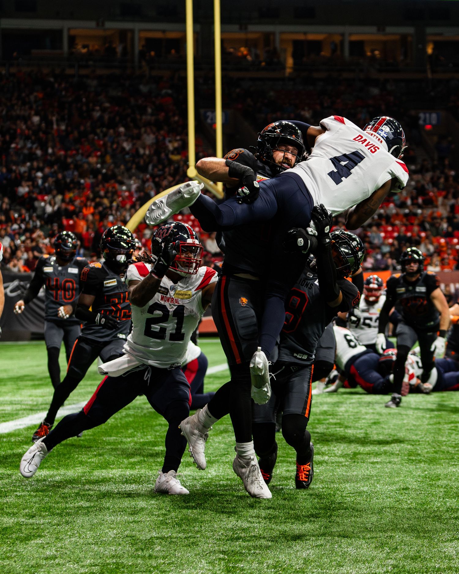 Football players collide mid-air during an intense CFL game, with player number 4 leaping near the end zone.