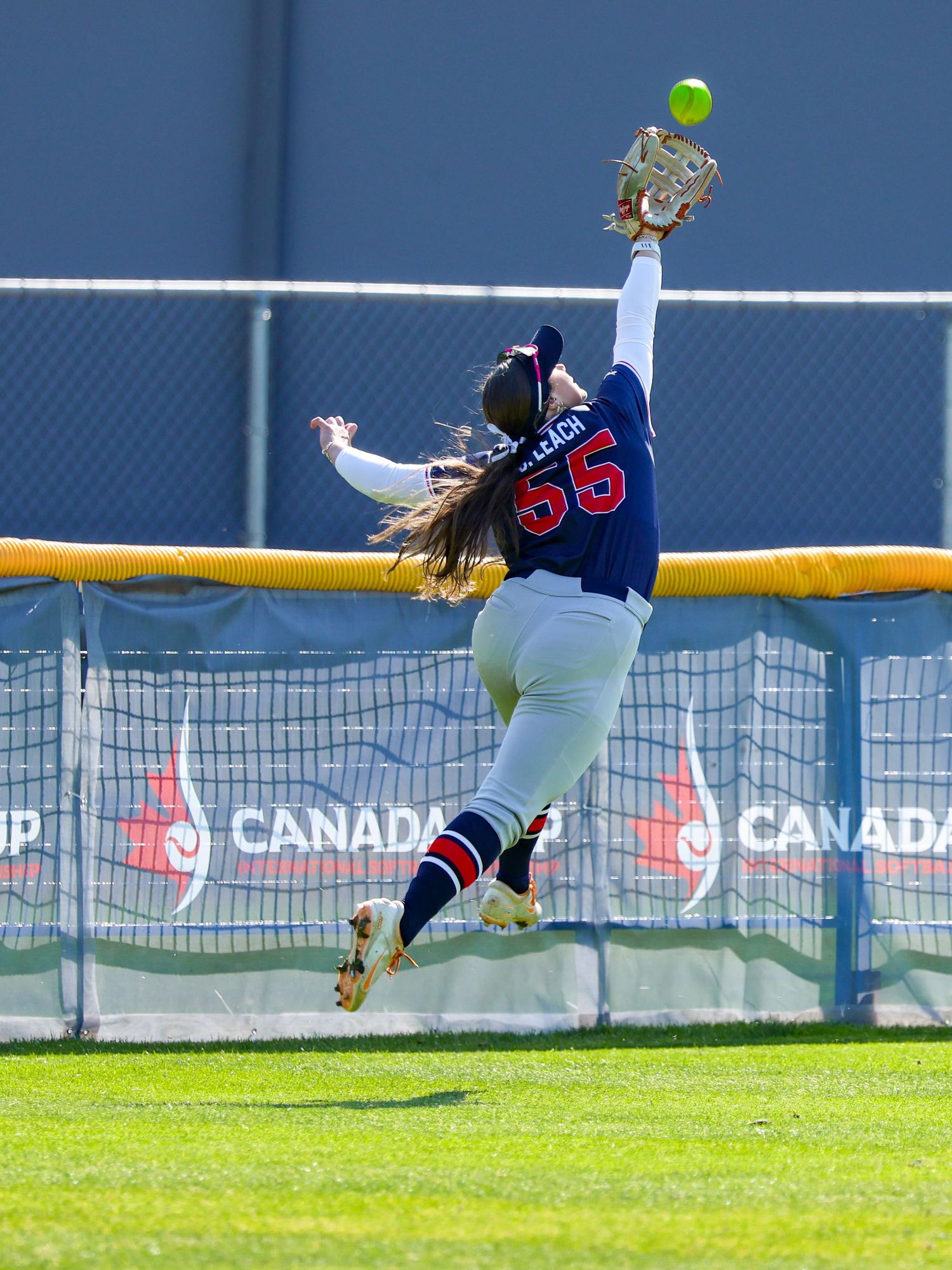 Softball player #55 leaps to make a spectacular catch at the outfield wall during a Canada Cup game.