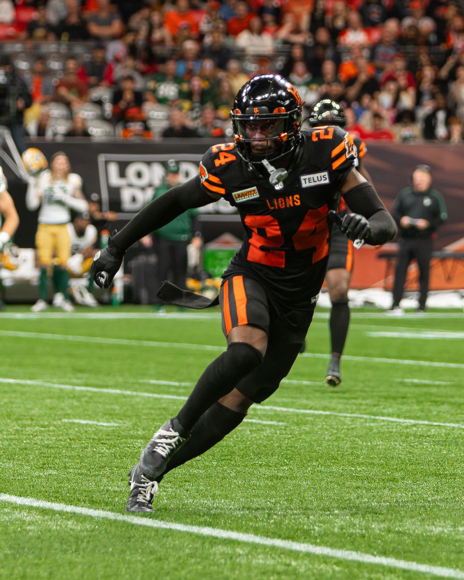 BC Lions player #24 in black and orange uniform sprints across the field during a CFL game.