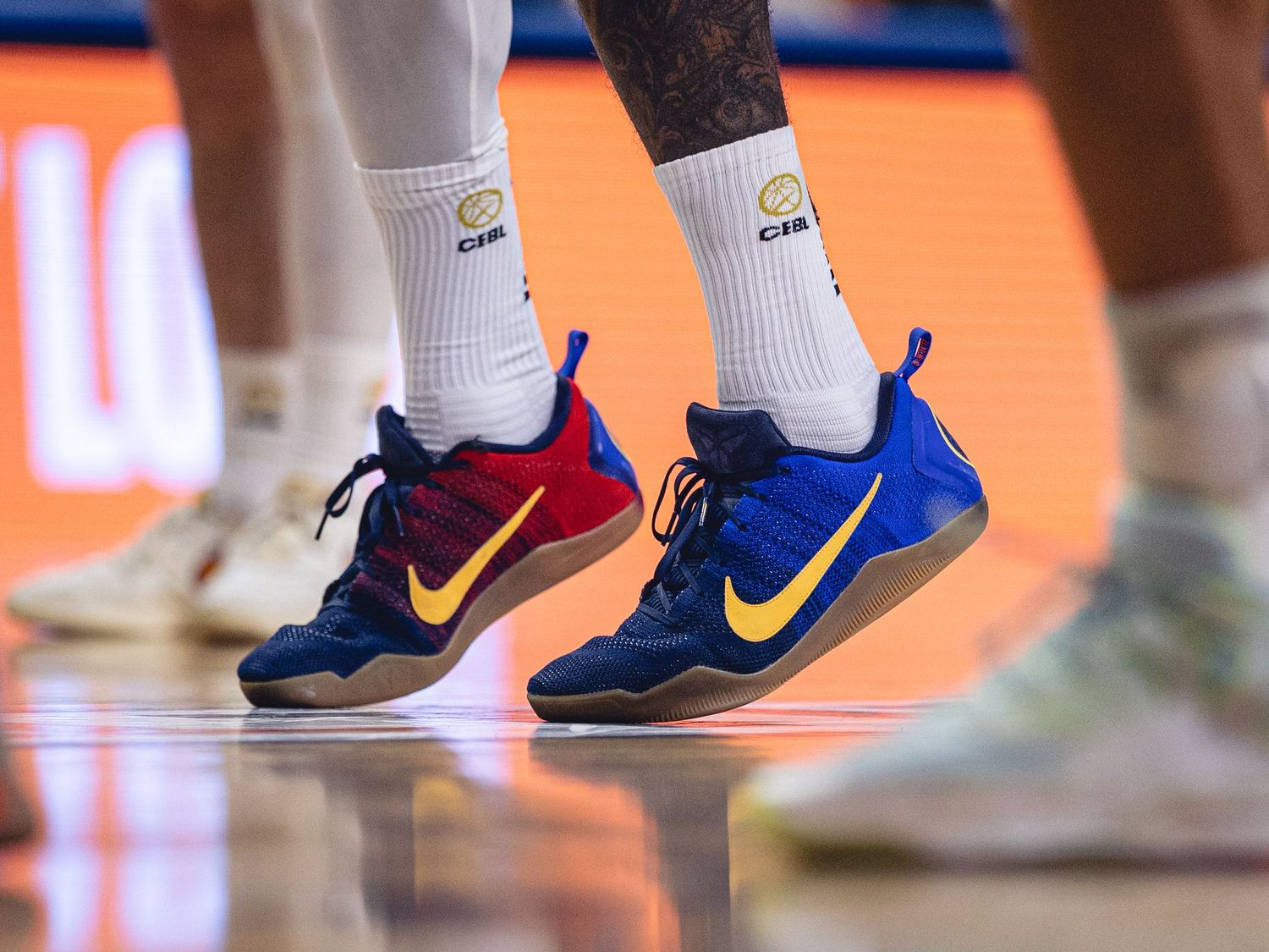 Close-up of basketball player wearing blue and red Nike sneakers with yellow swoosh on hardwood court.