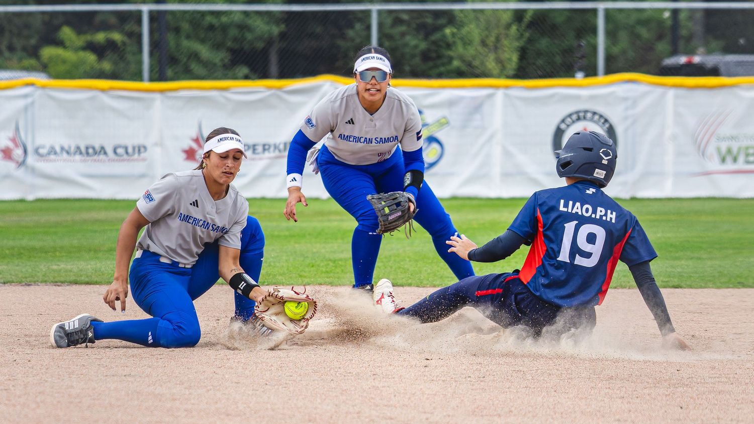 Softball player sliding into base during Canada Cup game as fielder attempts tag in competitive international tournament.