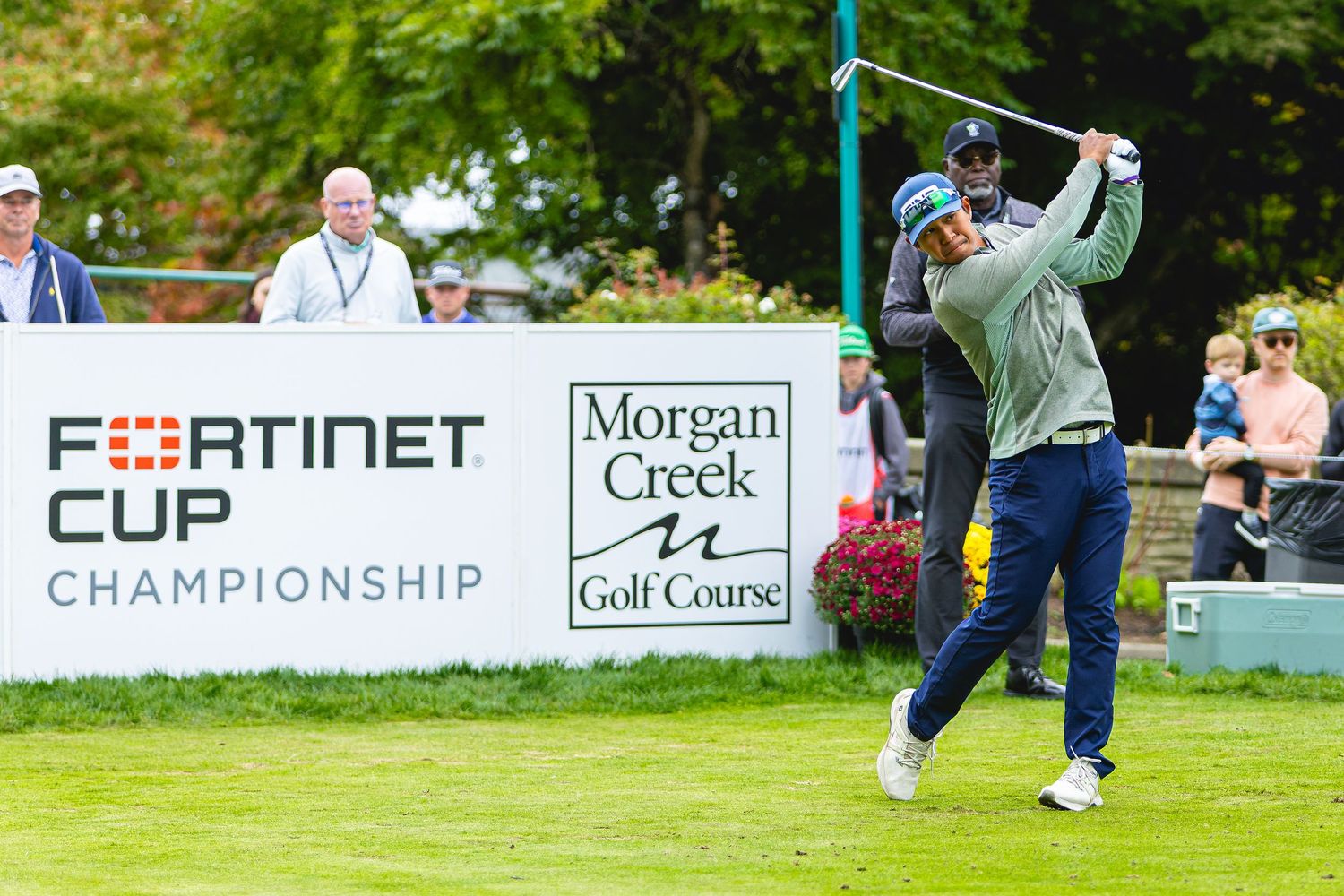 Golfer tees off at Fortinet Cup Championship at Morgan Creek Golf Course with spectators watching.