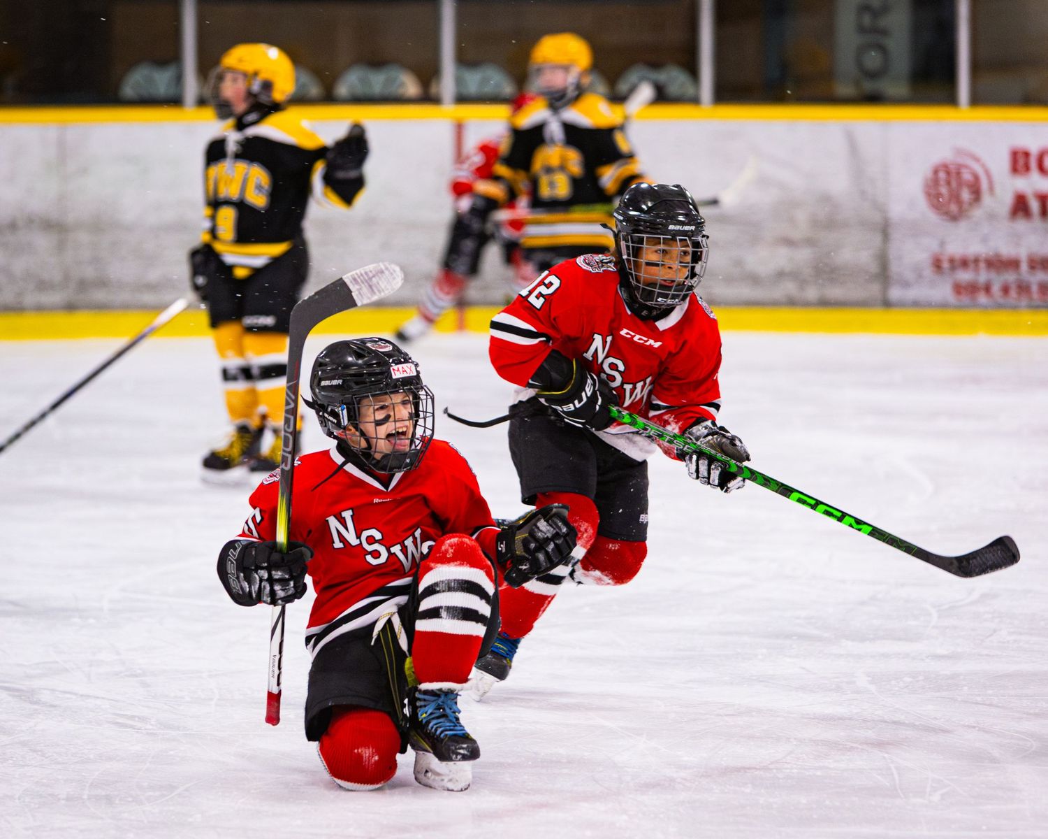 Two young hockey players in red uniforms skate aggressively during a youth ice hockey game.