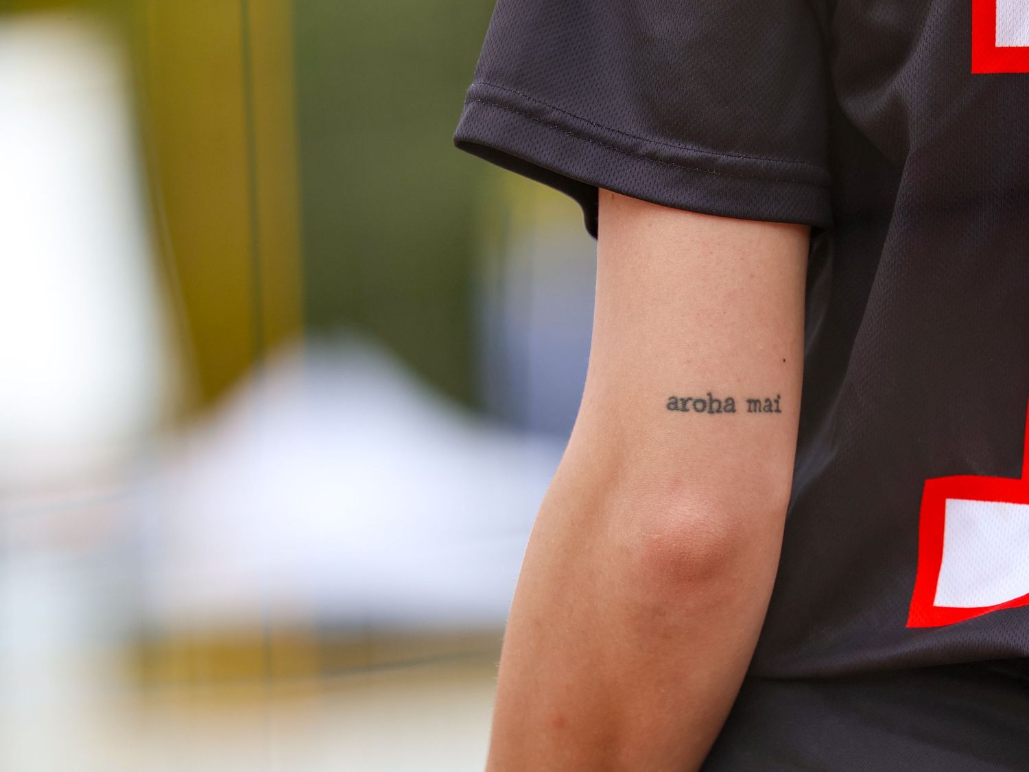 Close-up of a tattoo reading 'aroha nui' on the inner arm of an athlete wearing a dark jersey.
