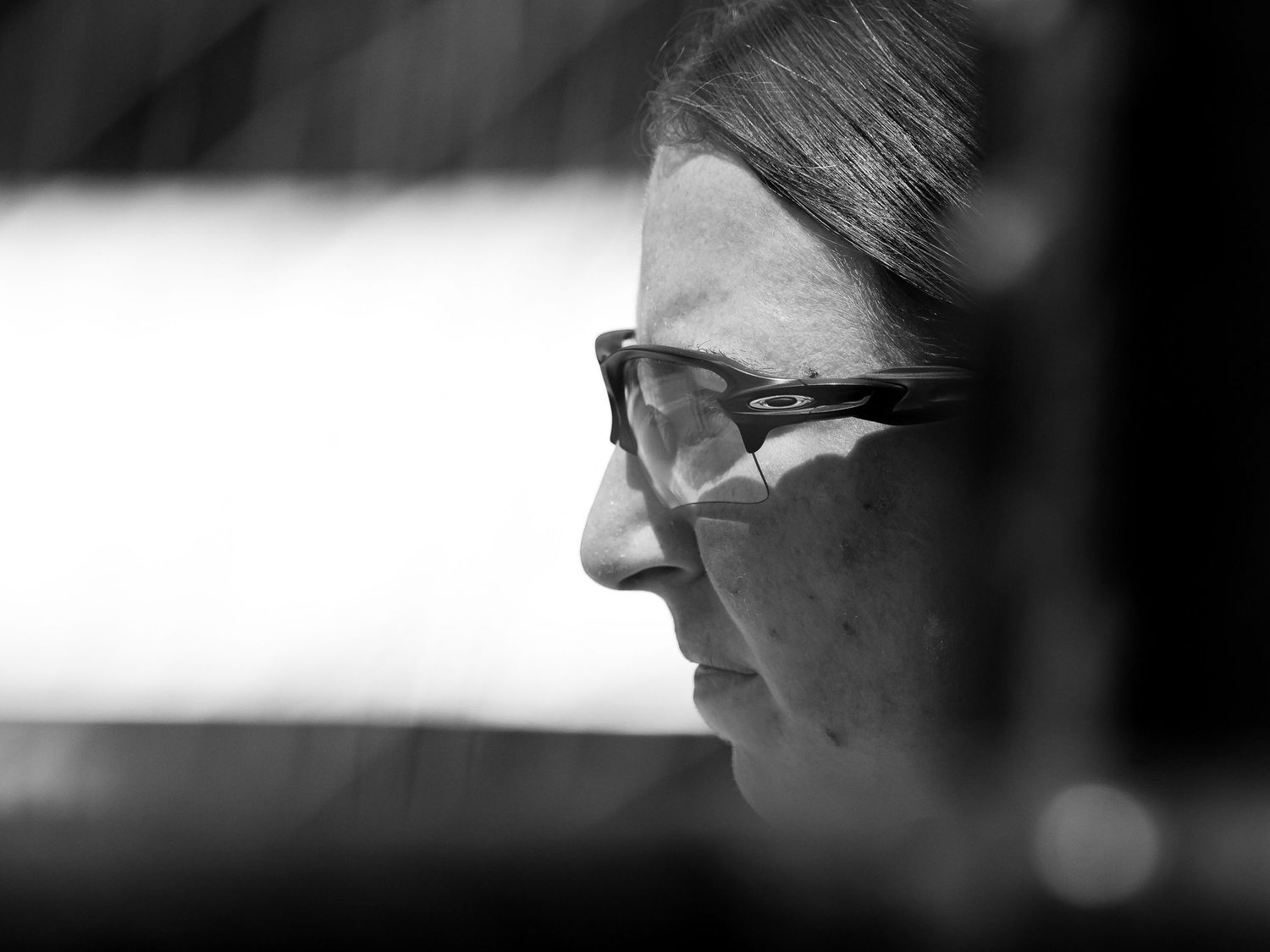 Black and white close-up profile portrait of a woman wearing glasses, with soft light highlighting her features.