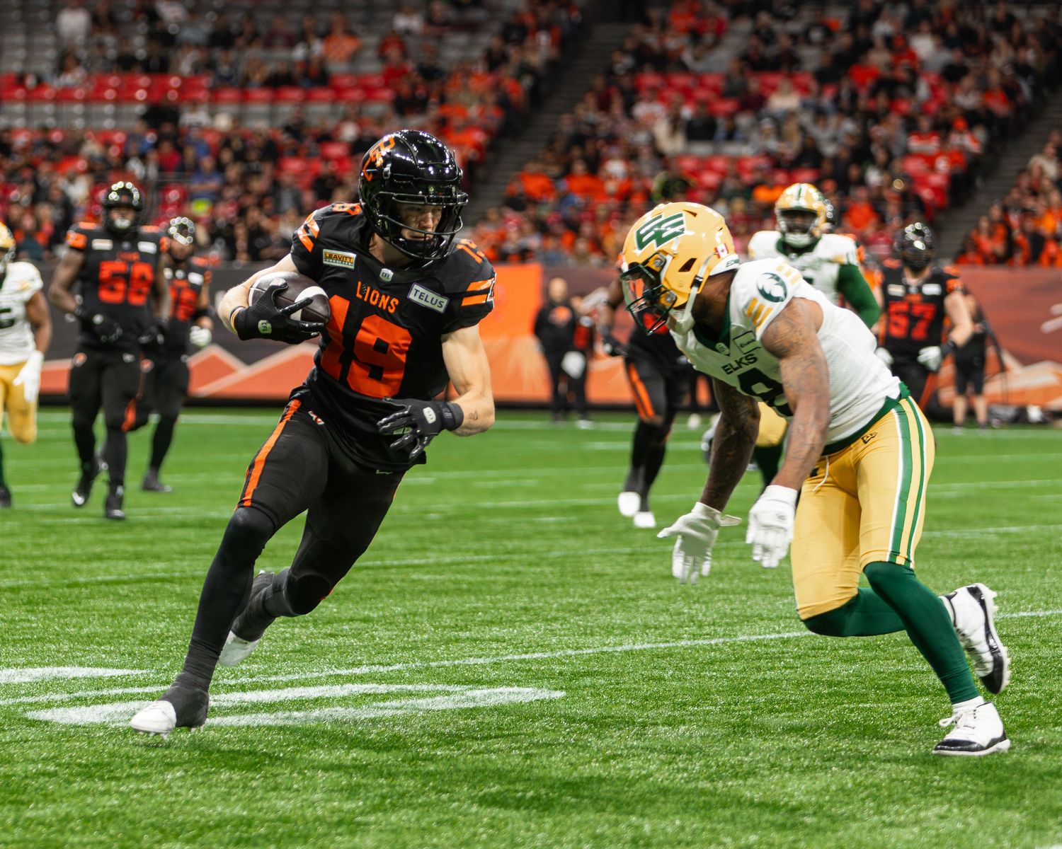 BC Lions player runs with the ball past an Edmonton Elks defender during a CFL game.