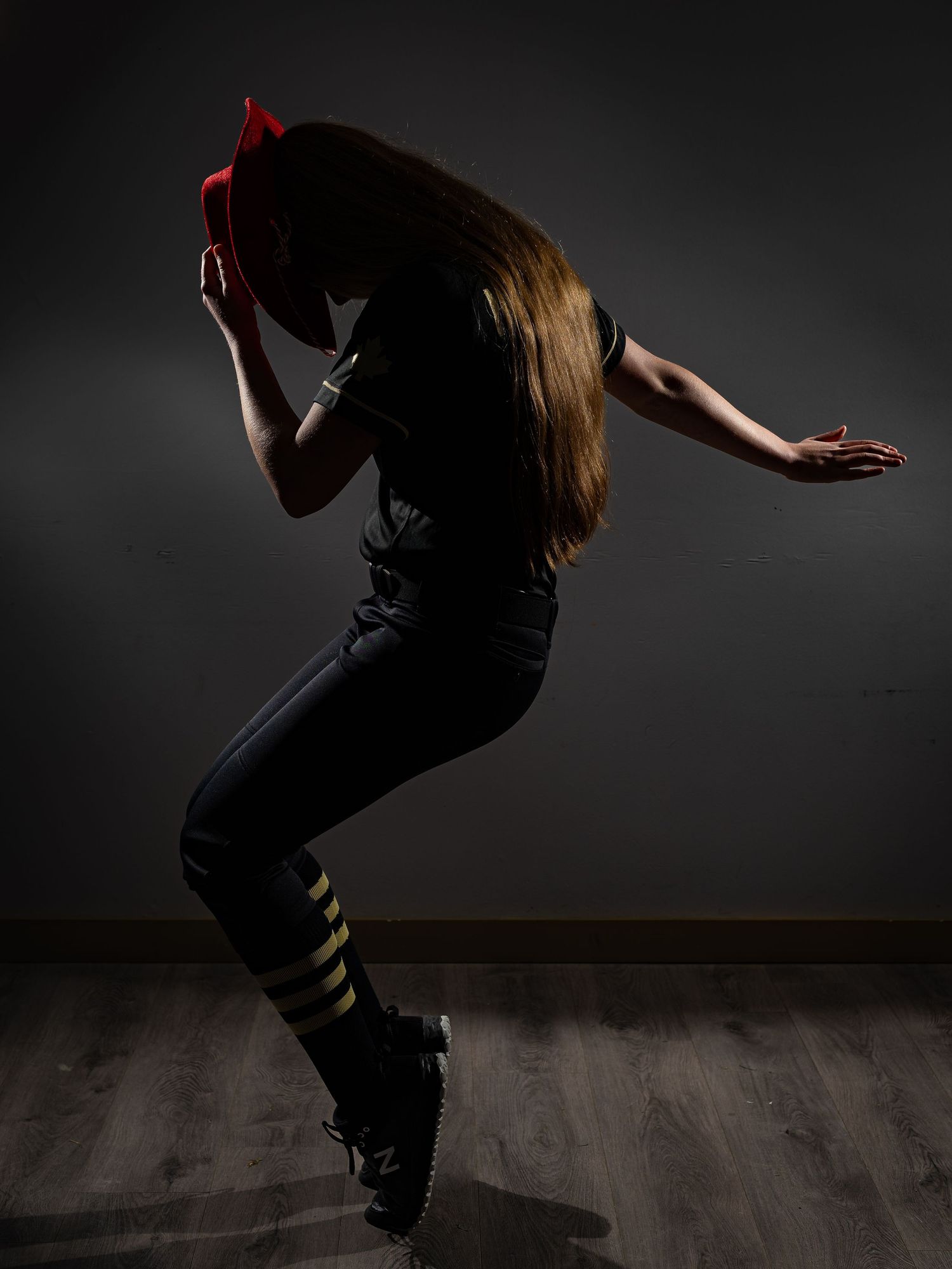 A dancer in black outfit with red bow poses dynamically against dark backdrop, hair flowing forward.