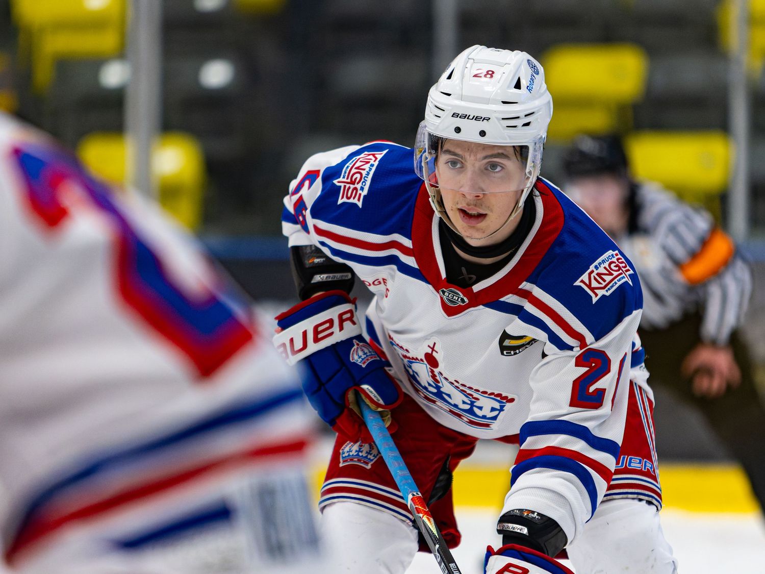 Ice hockey player in white uniform crouches at face-off during a professional hockey game on indoor rink.