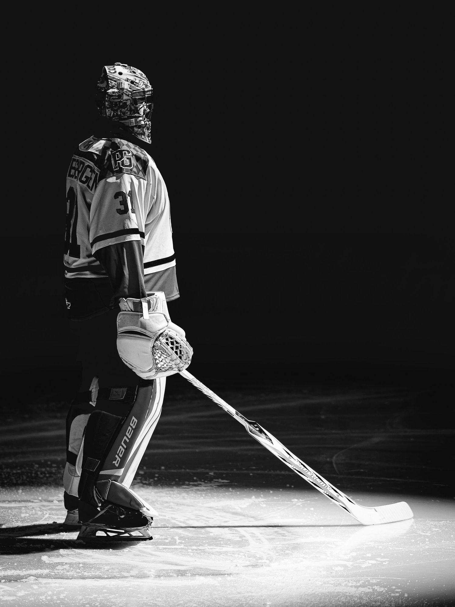 Black and white photo of hockey goalie #31 standing on ice rink holding stick, wearing full protective gear.