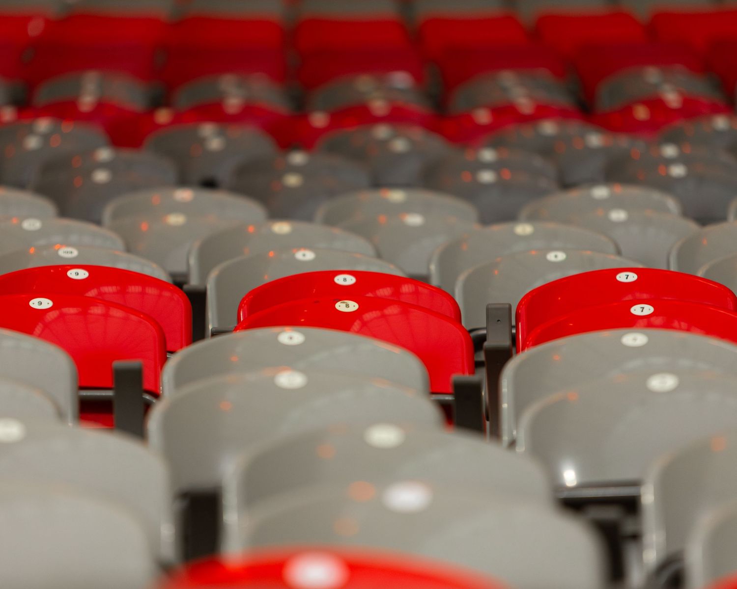 Rows of empty red and gray stadium seats arranged in alternating pattern at a sports arena.