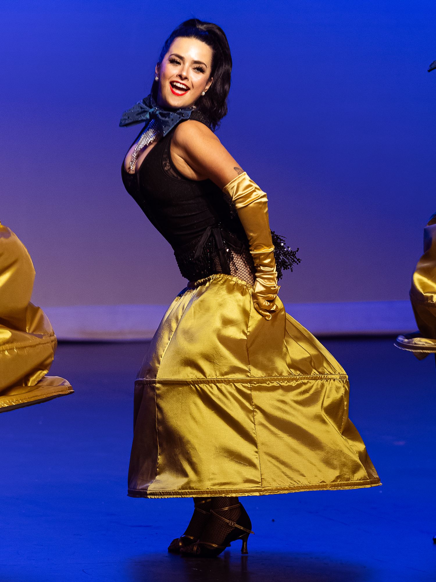 Dancer in gold satin skirt and gloves performs on stage under blue spotlight.