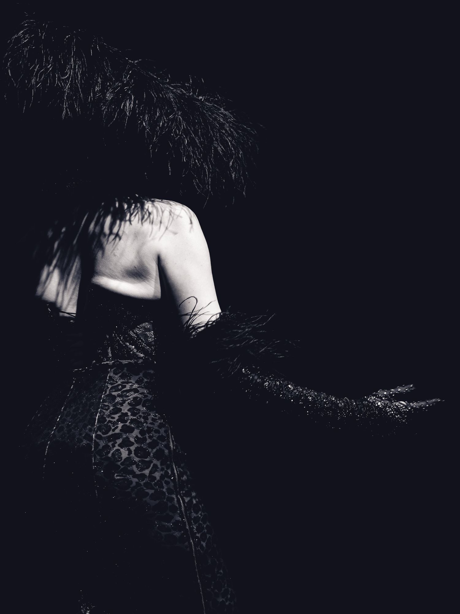 Black and white photo of a person in leopard print with feathered headpiece, dramatic dark background.