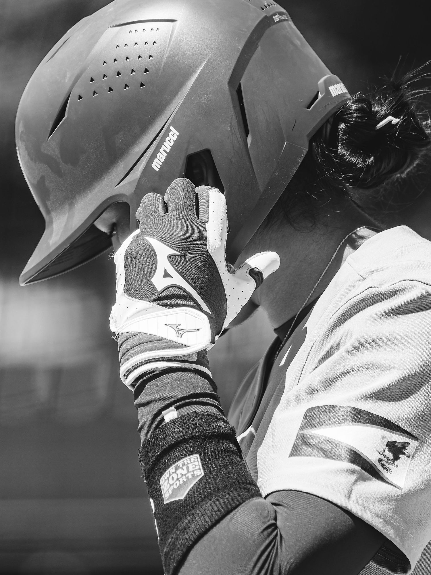 Black and white photo of a softball player adjusting their Mizuno batting glove and Rawlings helmet.