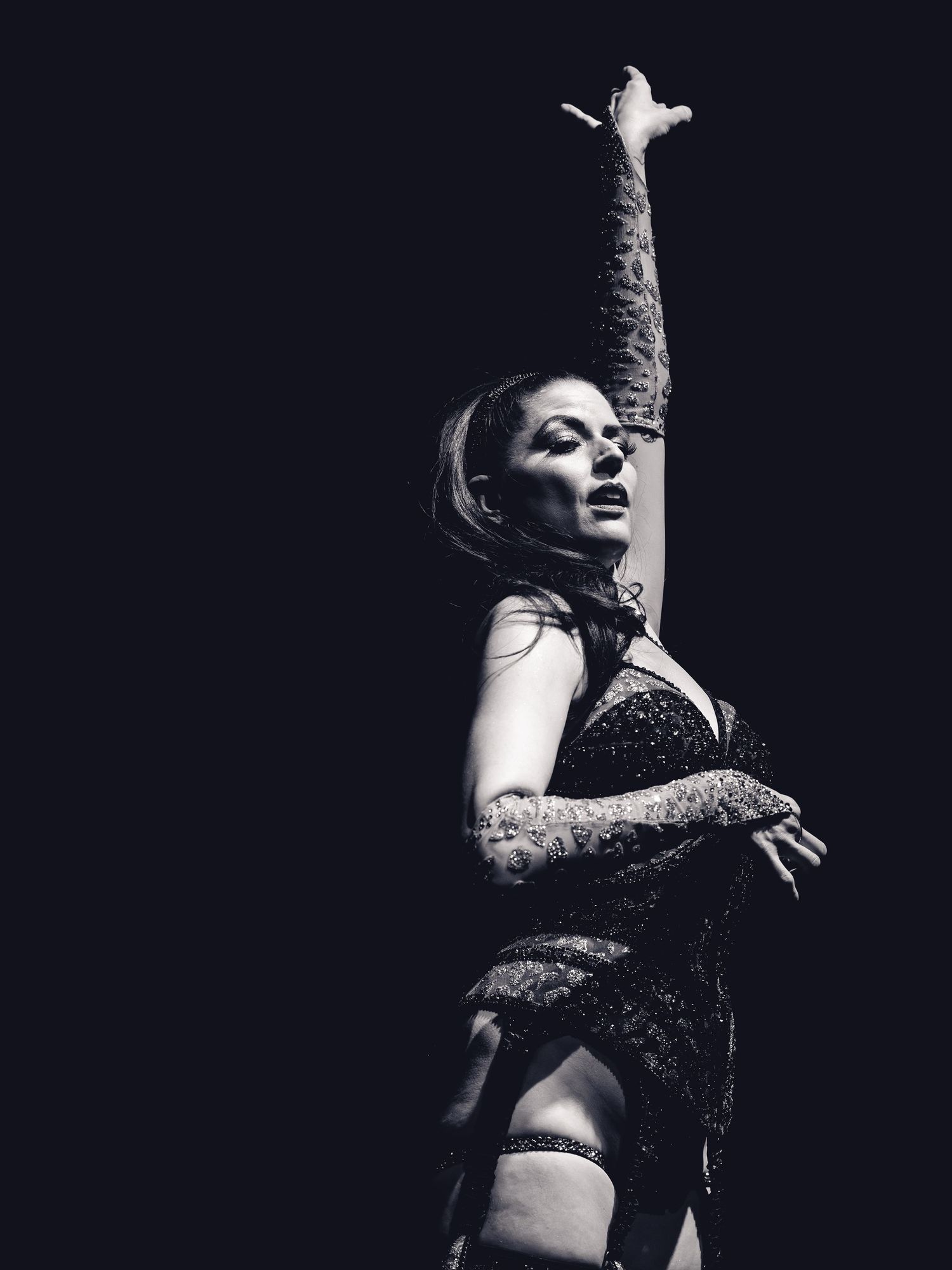 Black and white photo of a female performer in sequined costume striking a dramatic pose on stage.